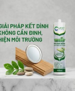 Một chai Keo đa năng V-Bond+ VCC 300ml đặt trên bệ đá cẩm thạch trắng, bên cạnh là một tấm gương nhỏ đang được dán vào một miếng gỗ sồi đánh bóng, không có đinh vít. Hình ảnh có các lá cây xanh tươi và logo VCC.