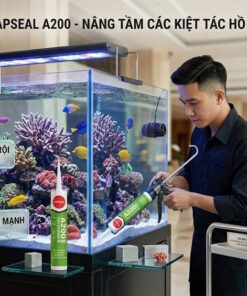 Ảnh chụp ngang về kỹ thuật viên VCC đang dùng súng bắn keo silicone axit Japseal A200 để dán một bể cá rạn san hô mặn. Bên cạnh là bảng hiệu kim loại liệt kê các tính năng: chống thấm, chịu nhiệt vượt trội, bám dính mạnh mẽ, khô nhanh, thân thiện môi trường. Thùng hàng và ống keo Japseal A200 cũng được trưng bày rõ ràng.