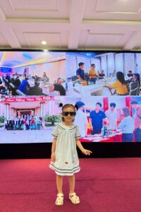 Bé gái đáng yêu là con em của nhân viên tự tin tạo dáng trên thảm đỏ trước màn hình LED trình chiếu hoạt động công ty tại lễ kỷ niệm thành lập VCC.