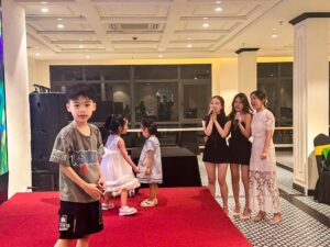 Các em nhỏ vô tư vui đùa trên sân khấu bên cạnh các nữ cán bộ nhân viên đang biểu diễn ca nhạc tại lễ kỷ niệm thành lập VCC.