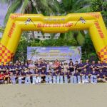 Group of People in Purple Shirts Posing on a Beach During a Team building Event Under a Yellow Inflatable Arch That Says race on Top with team Building Letters in Front  Vcc Sealant   Sản Xuất Phân Phối Keo Silicone Và Chất Kết Dính Chuyên Nghiệp
