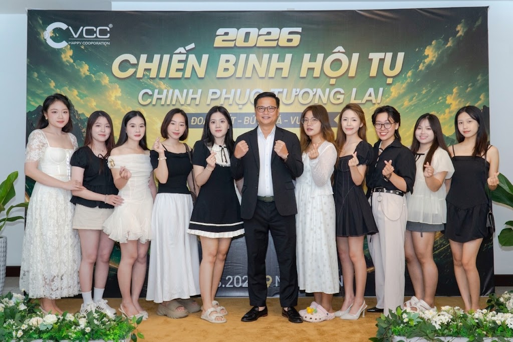 Group of people, mostly young women, posing with fists raised in front of a green event banner reading 2026 and Vietnamese text.